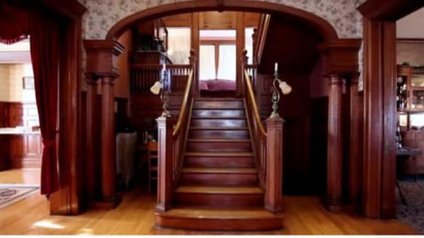 A grand wooden staircase with ornate railings, leading to a landing area with a view of the outside. - 1897 Beekman House (Dundee)