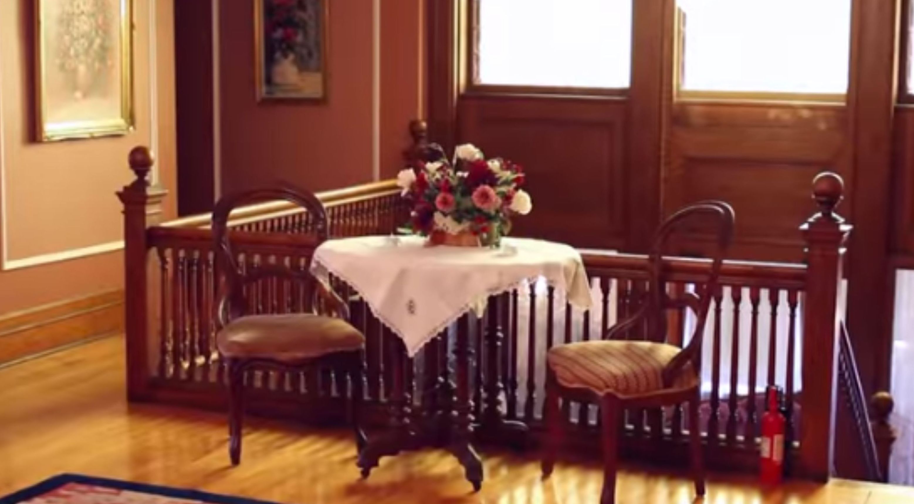 A dining area with a table set for two, wooden chairs, and a floral centerpiece.
