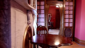 A hallway with a marble column, a wooden table with chairs, and a room with bookshelves and a mirror. - 1897 Beekman House (Dundee)