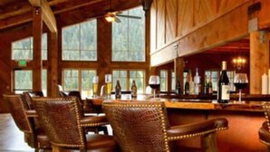 A rustic interior with wooden beams, large windows, wicker chairs, and a bar area.