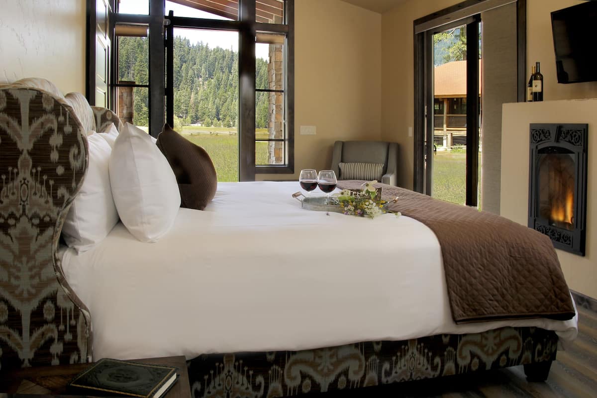 Un dormitorio con una cama grande, una chimenea y vistas a un bosque a través de una puerta corrediza.