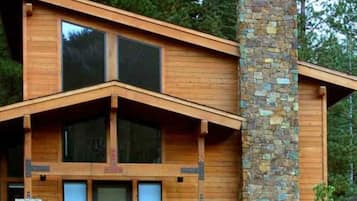 Eine moderne Blockhütte mit einem Steinkamin, großen Fenstern und einer Veranda mit roten Stühlen.