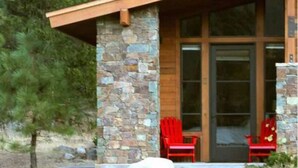 A modern building with a stone facade, large glass doors, and a covered porch area with red chairs.
