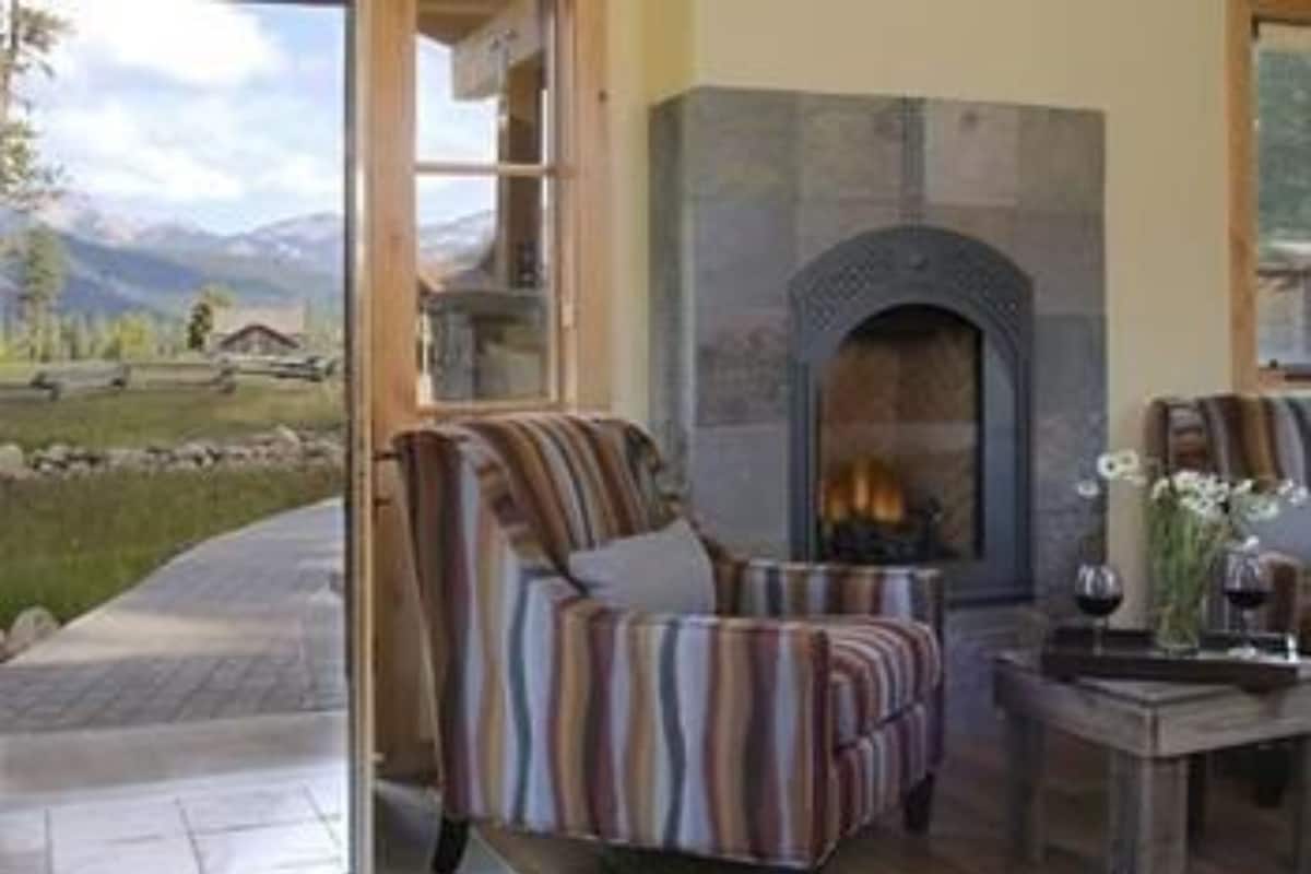 Un salón acogedor con chimenea, sillones a rayas y vistas a un paisaje montañoso a través de amplios ventanales.