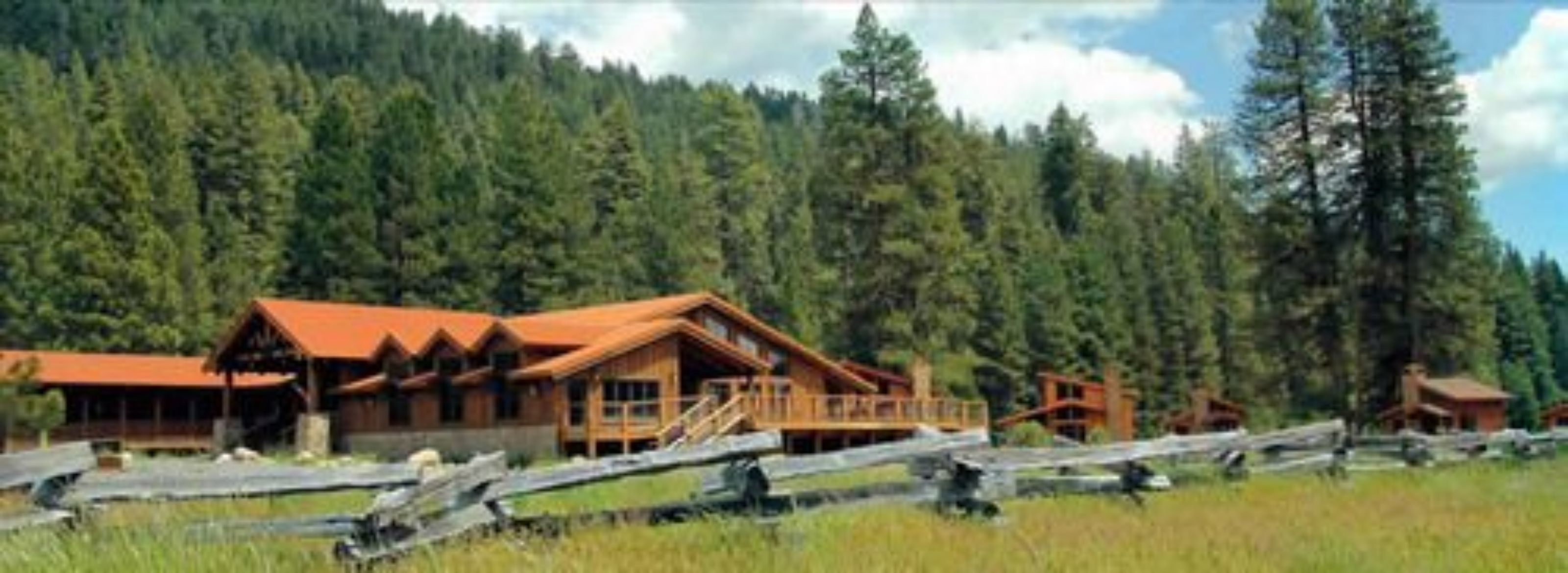 A lodge with multiple wooden cabins, a covered deck, and a forested backdrop.