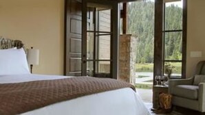 A bedroom with a large bed, a nightstand, a lamp, and a view of a forest through a large window.