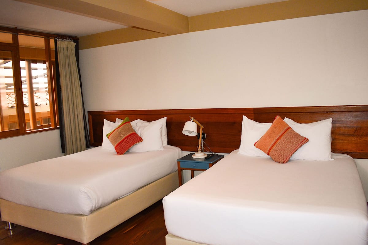 Dos camas individuales con sábanas blancas, cabeceros de madera y almohadones decorativos.