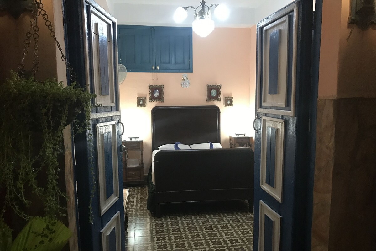 Un dormitorio con cama, mesita de noche y un ventilador de pared.