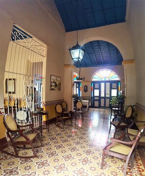 A spacious lobby with patterned tile flooring, wooden chairs, a dining area with a table and chairs, and a large arched doorway with stained glass. - Hostal Los Vitrales (Remedios)