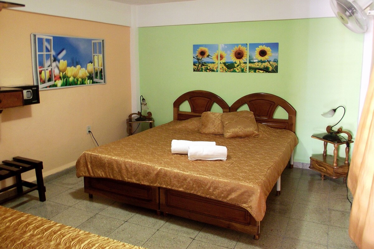 Un dormitorio con cama, mesita de noche, lámpara y ventilador de pared.