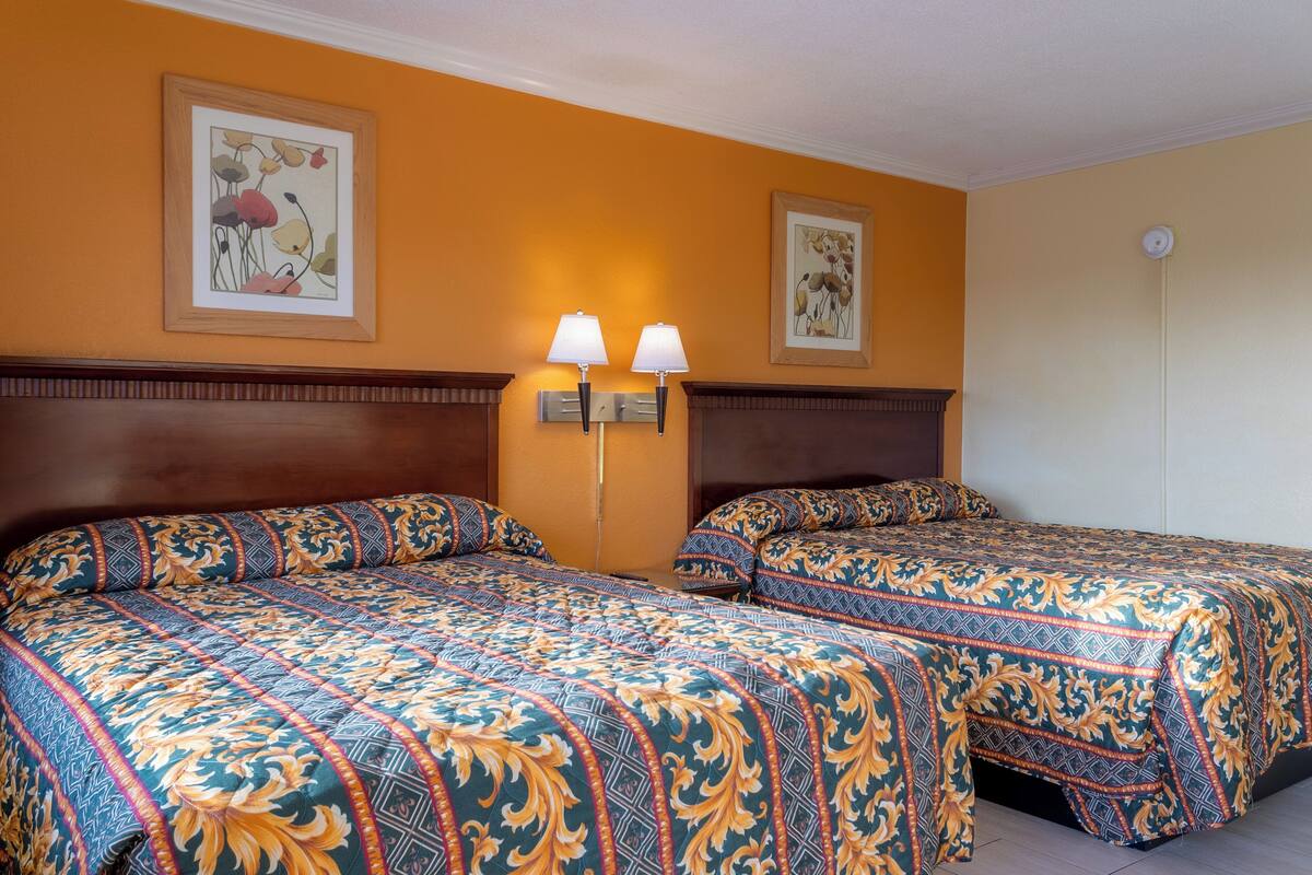 Une chambre d’hôtel avec deux lits, chacun agrémenté de draps à motifs, d’une tête de lit, de lampes fixées au mur et d’œuvres d’art encadrées accrochées aux murs.