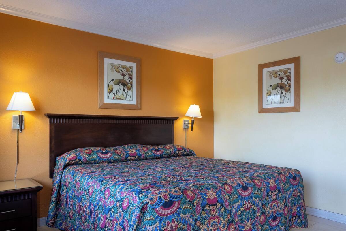 Une chambre d’hôtel avec un grand lit, deux lampes fixées au mur et deux tableaux encadrés accrochés aux murs.