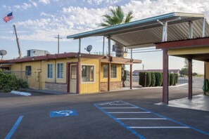 A small building with a yellow facade, a covered parking area, and a handicapped parking space. - Kings Rest Motel (Lemoore)