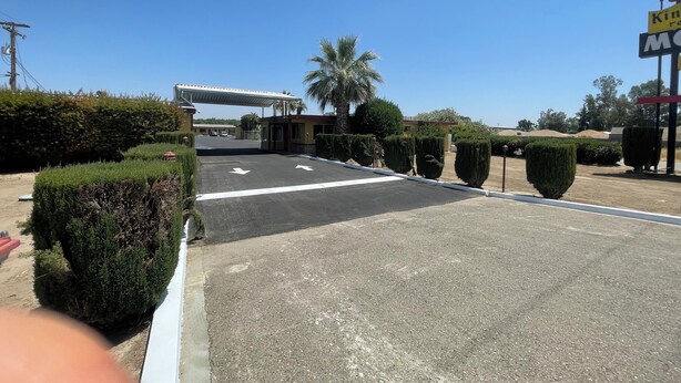A parking area with directional arrows, a covered entrance, and well-maintained landscaping. - Kings Rest Motel (Lemoore)
