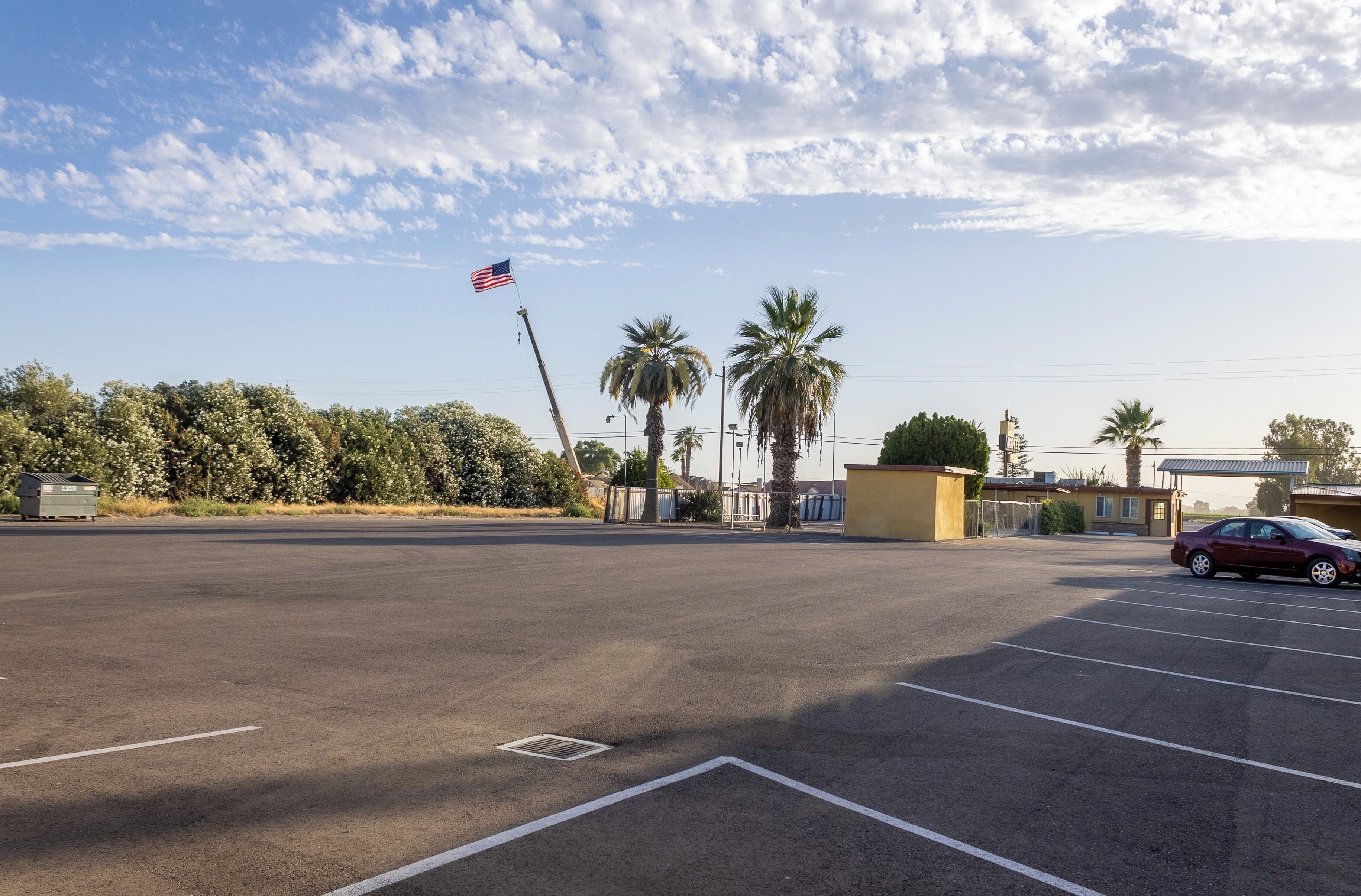 A parking lot with a red car, palm trees, and an American flag.