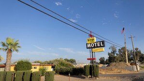 A motel sign with an American flag, surrounded by a palm tree and a building in the background. - Kings Rest Motel (Lemoore)