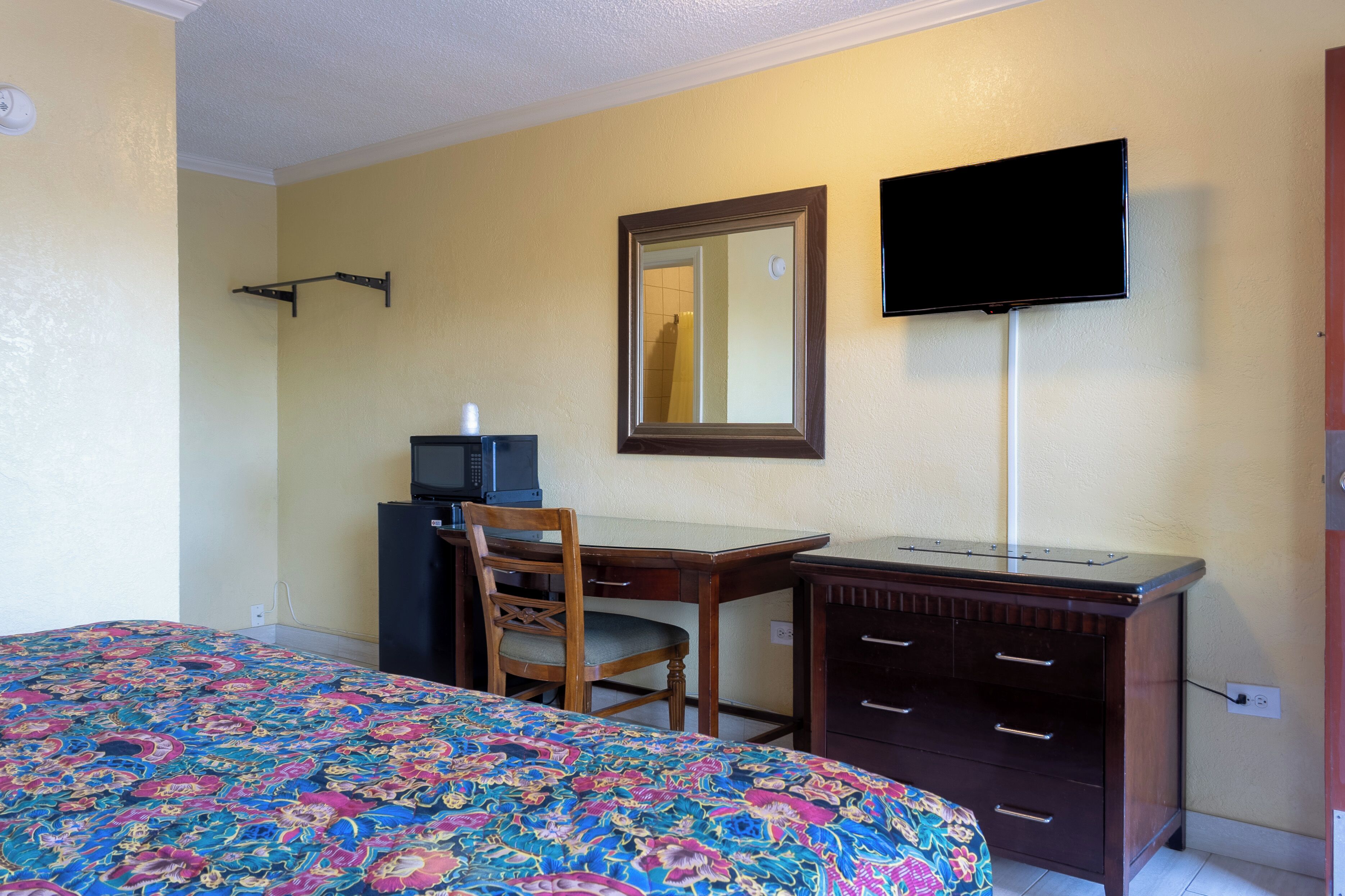 A hotel room with a bed, a desk, a chair, a television, and a dresser.