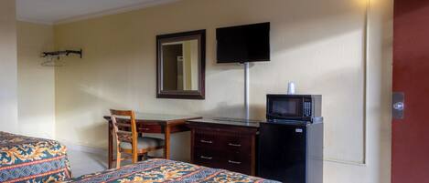 Una habitación de hotel con cama, un escritorio con silla, televisión y microondas.