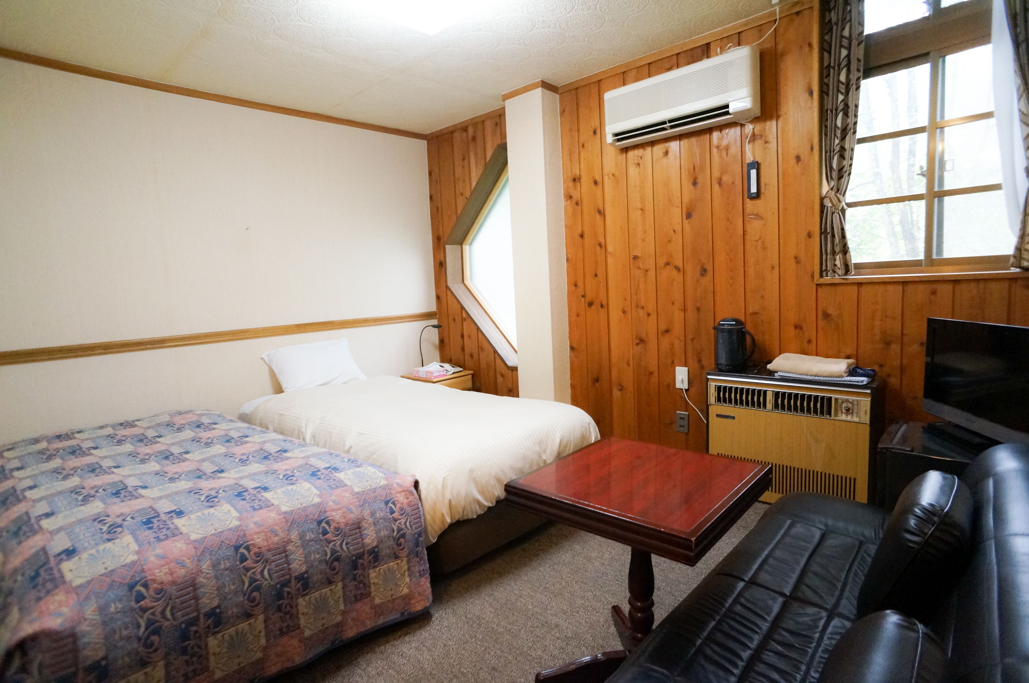 Ein Zimmer mit Holzwänden, einem Bett mit einem gemusterten Quilt, einem kleinen Tisch, einer Couch und einem Heizkörper.