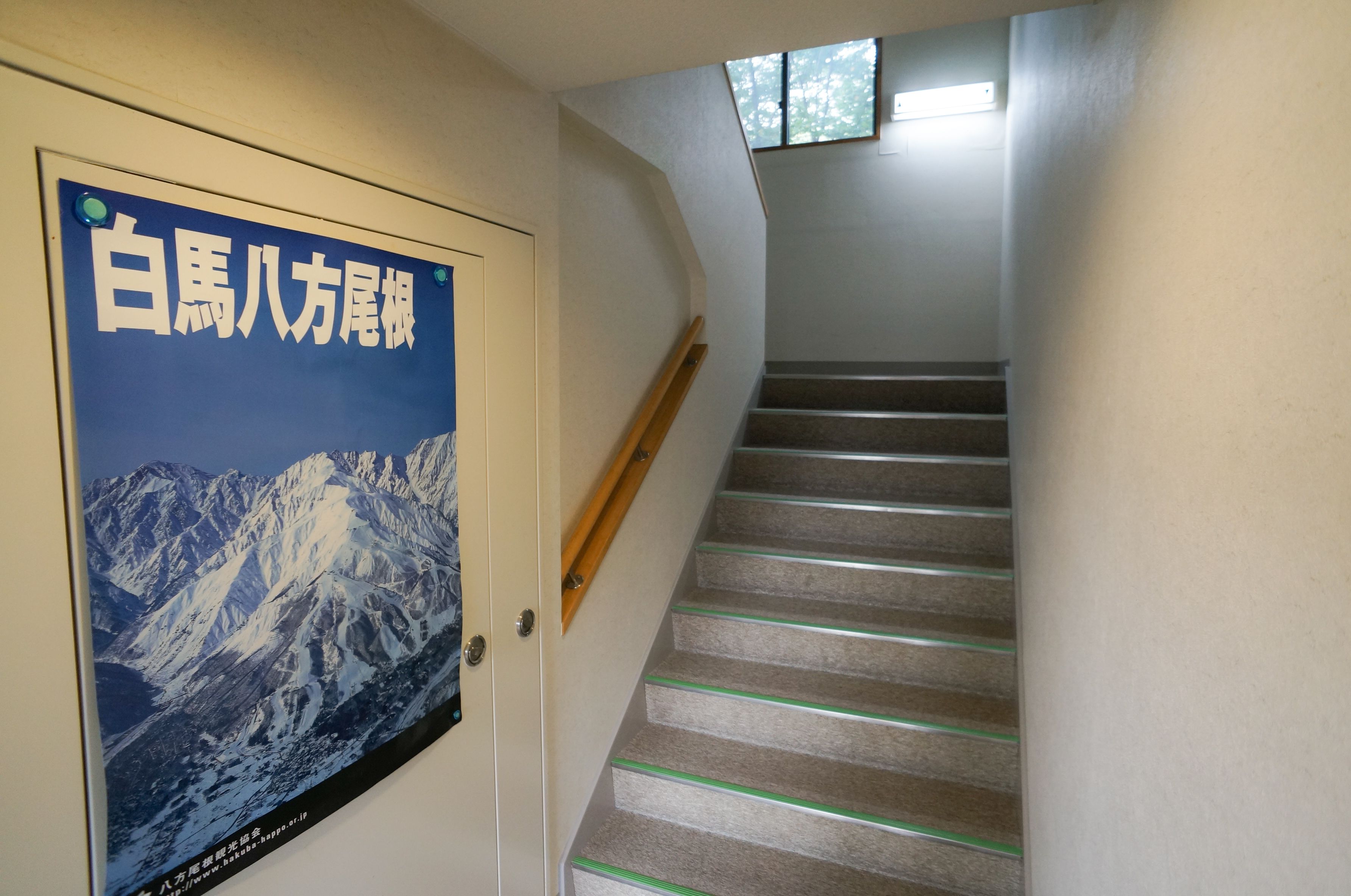 Una escalera con barandilla de madera y un cartel con una cordillera en la pared.