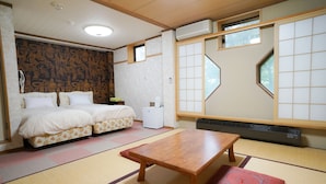 Una habitación japonesa tradicional con suelo de tatami, una mesa de madera, dos camas con ropa de cama floral y una ventana con pantalla shoji.