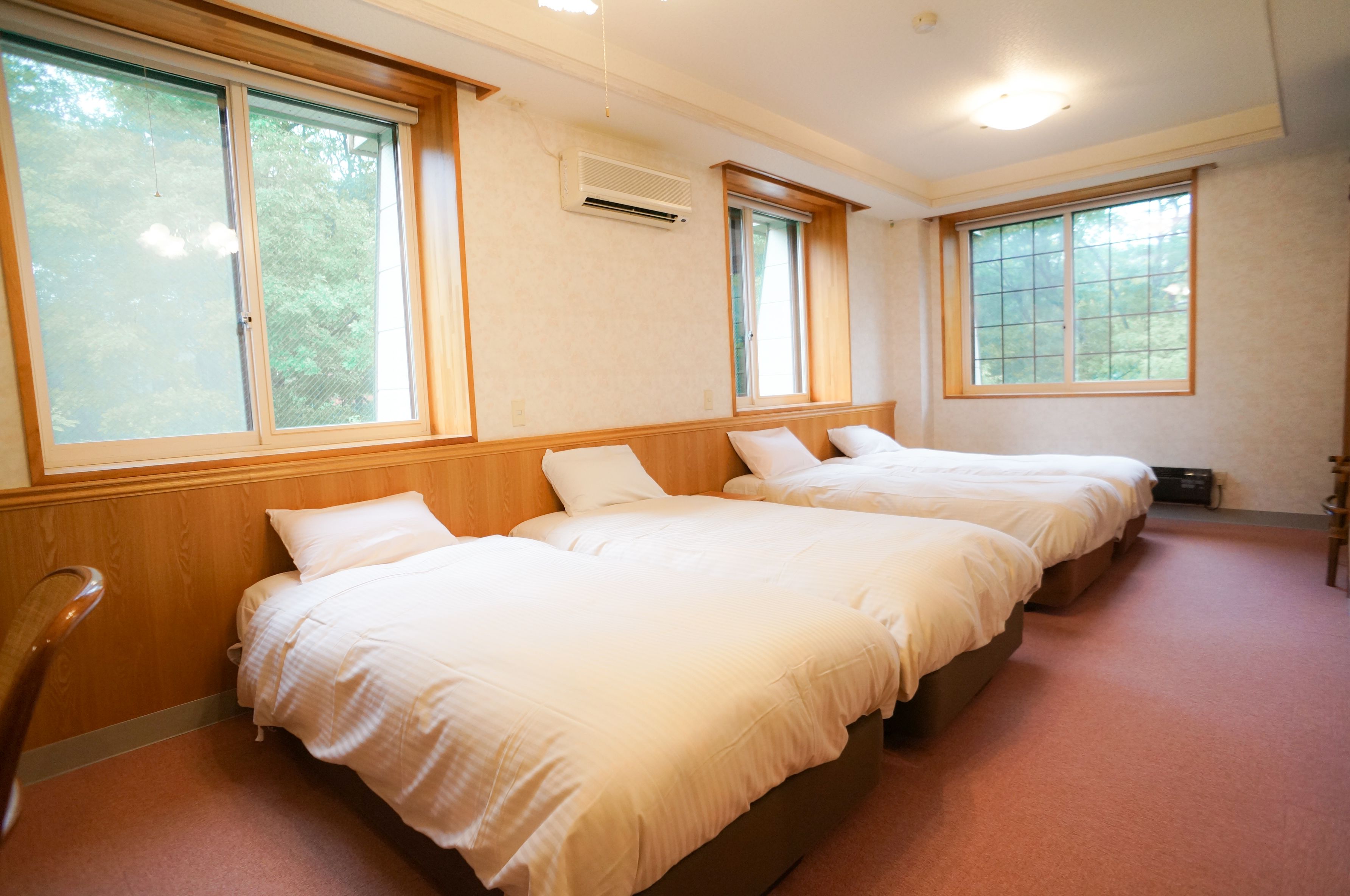 Una camera d'albergo con tre letti, ampie finestre e un condizionatore.