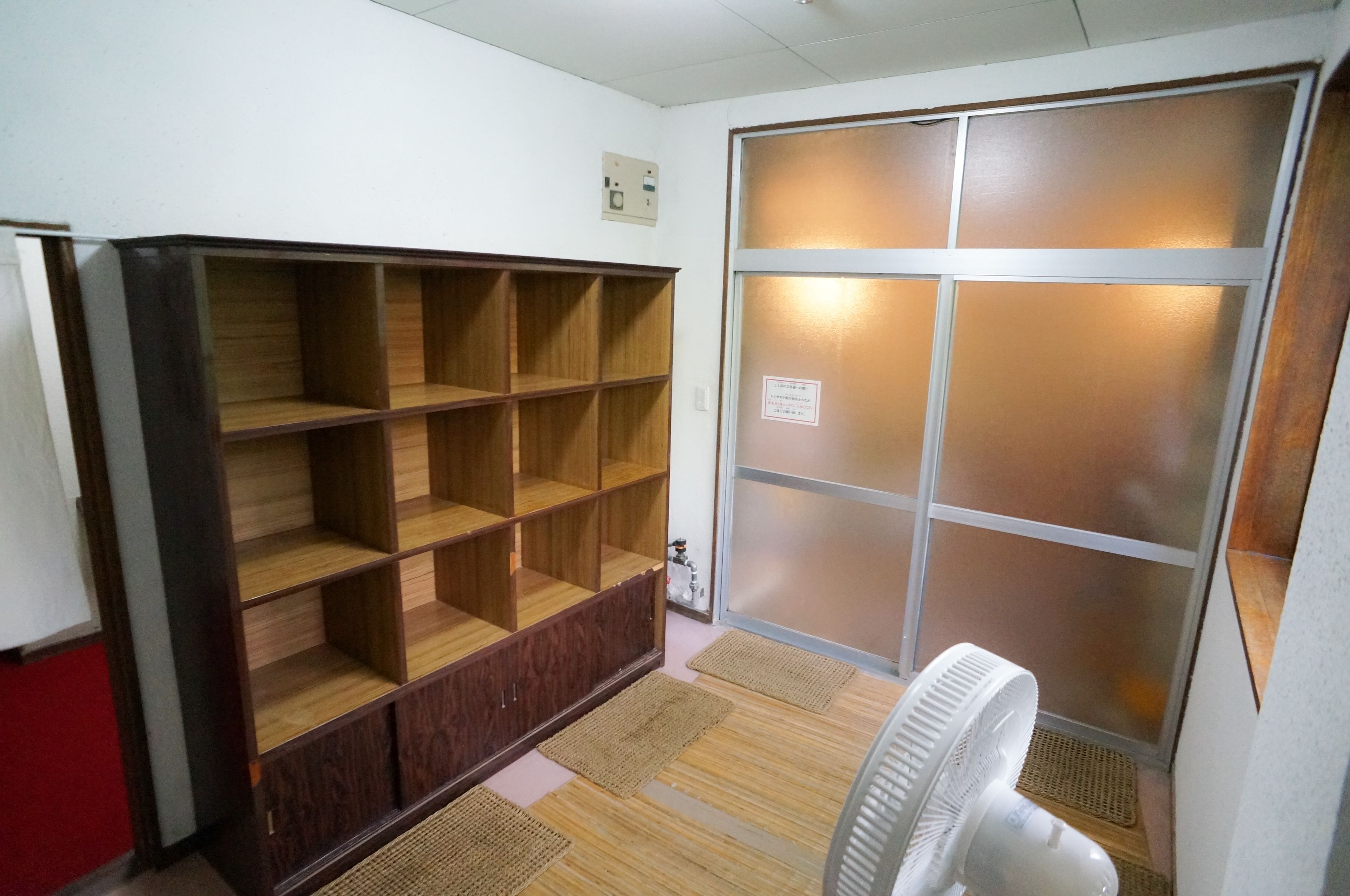 A room with a large wooden shelving unit, a sliding glass door, and a white standing fan.