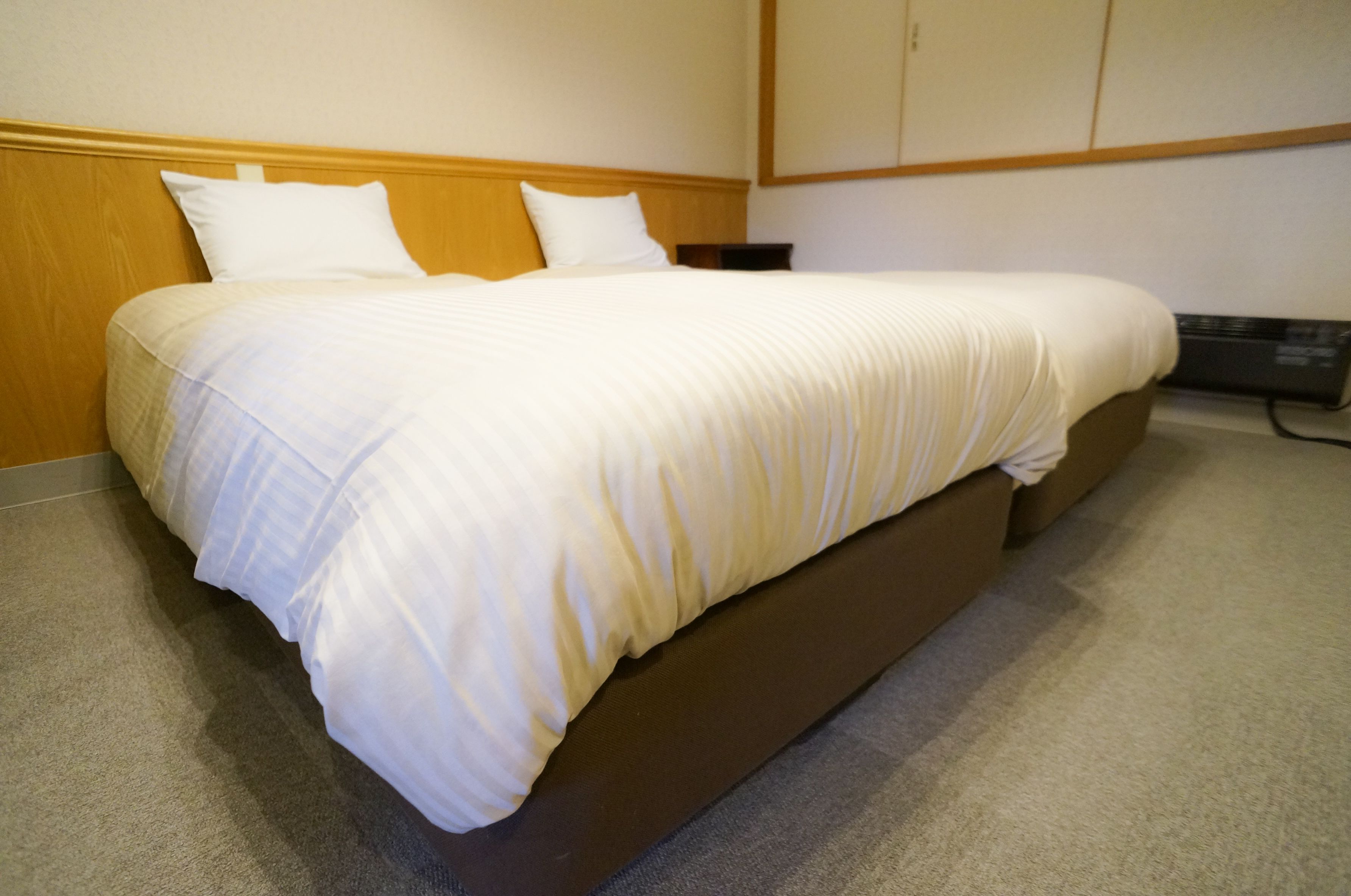 A neatly made bed with a wooden headboard and a white comforter.