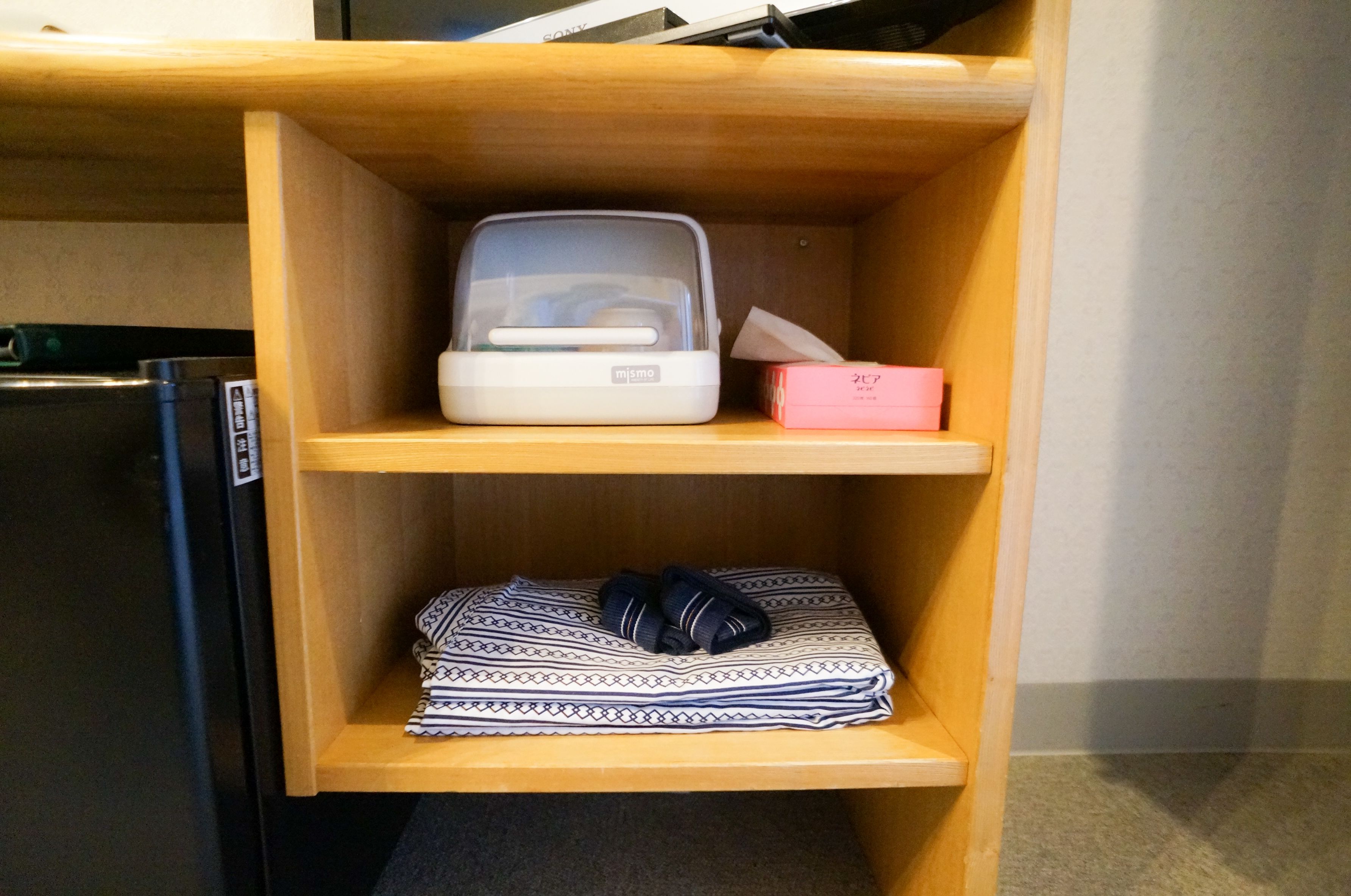 A wooden shelf unit with a microwave, a tissue box, and folded towels.