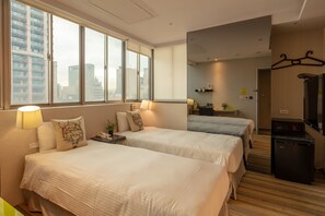 Quarto de hotel com duas camas, uma mesa, um frigorífico e uma televisão.
