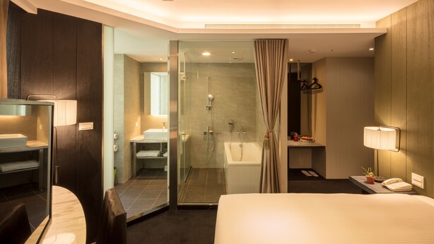 A hotel room with a bed, a glass-enclosed shower, a vanity with a mirror, and a bedside table with a lamp and a phone. - Finders Hotel-Fu Qian (Taipei)