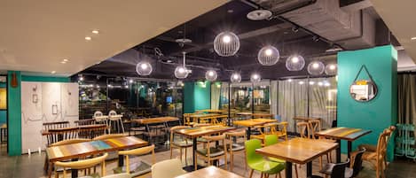 Interior de restaurante com mesas e cadeiras de madeira, luminárias pendentes e uma parede de destaque em tom verde-água.