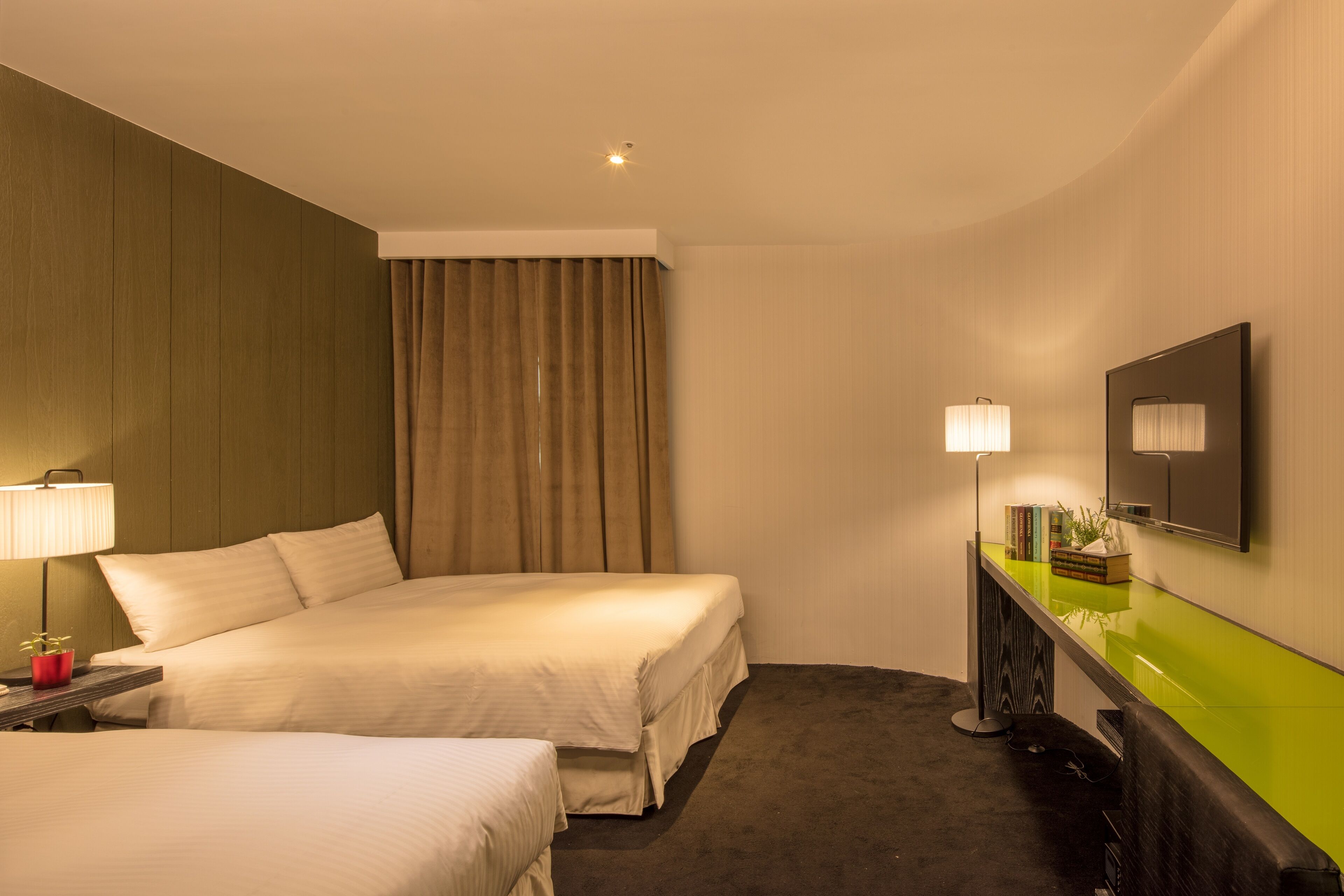 Une chambre d’hôtel avec deux lits, un bureau avec une lampe, un miroir et un comptoir vert.