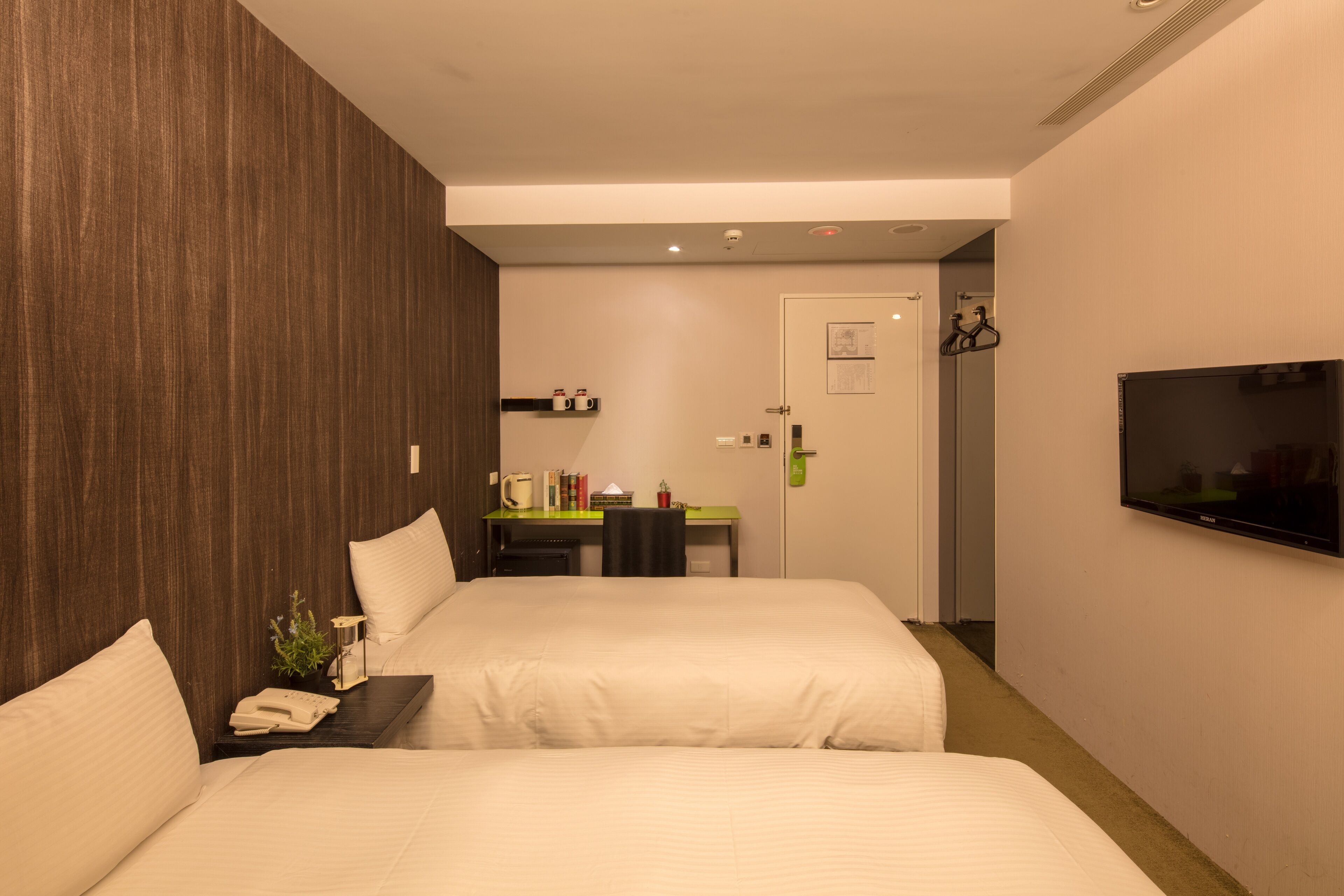 A hotel room with two beds, a desk, a chair, a television, and a door.