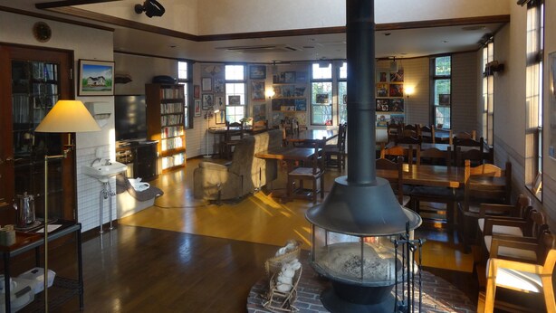 Un interior acogedor con un horno de leña en el centro, muebles de madera y una estantería llena de libros.