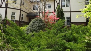 Un edificio tradicional con fachada simétrica, numerosas ventanas y un jardín bien cuidado con arbustos y plantas florecientes.
