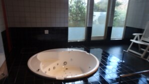 Un baño con una bañera grande, suelo de baldosas negras y una silla blanca cerca de la ventana.