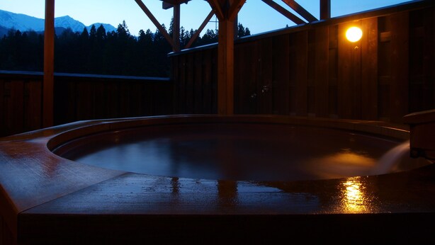A wooden hot tub under a wooden pergola with a view of mountains in the background. - Hakuba Hotel Hana no Sato (Hakuba)