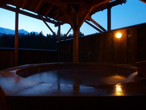 Una bañera de hidromasaje de madera bajo una pérgola de madera, con vistas a montañas al fondo.