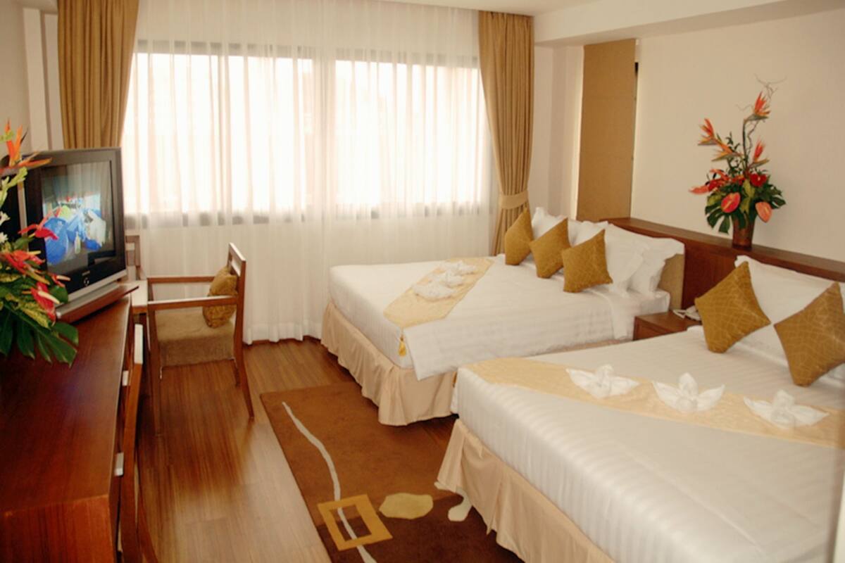 Ein Hotelzimmer mit zwei Betten, einem Fernseher, einem Schreibtisch und einem fenster mit Vorhängen.