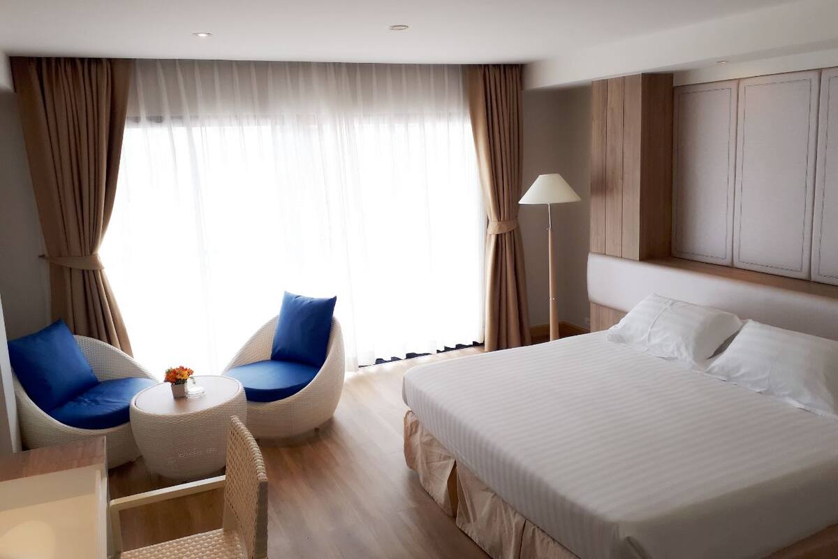 Ein Hotelzimmer mit einem großen Bett, zwei blauen Stühlen, einem kleinen runden Tisch und einer Lampe.