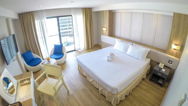 A hotel room with a large bed, a desk with a chair, a TV, and a balcony with curtains. - Hiran Residence (Patong)