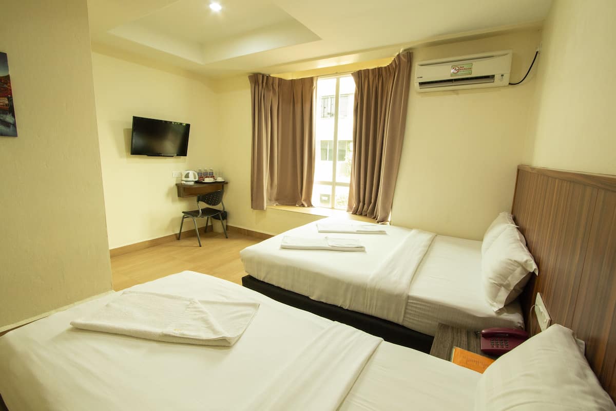 A hotel room with two beds, a desk, a television, and an air conditioning unit.