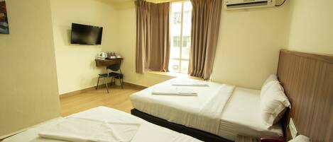 A hotel room with two beds, a desk, a television, and an air conditioning unit.