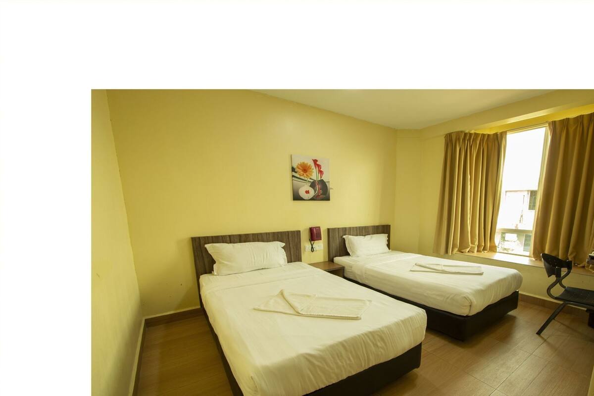 A hotel room with two beds, a painting on the wall, a window with curtains, and a chair.