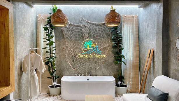 A modern bathroom with a freestanding bathtub, a white sofa, and a check-in sign. - Check-in Resort Koh Larn (Koh Lan)