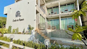 A modern hotel with a "Check-in Resort" sign, a multi-level balcony with seating, and a landscaped garden with cacti and shrubs. - Check-in Resort Koh Larn (Koh Lan)