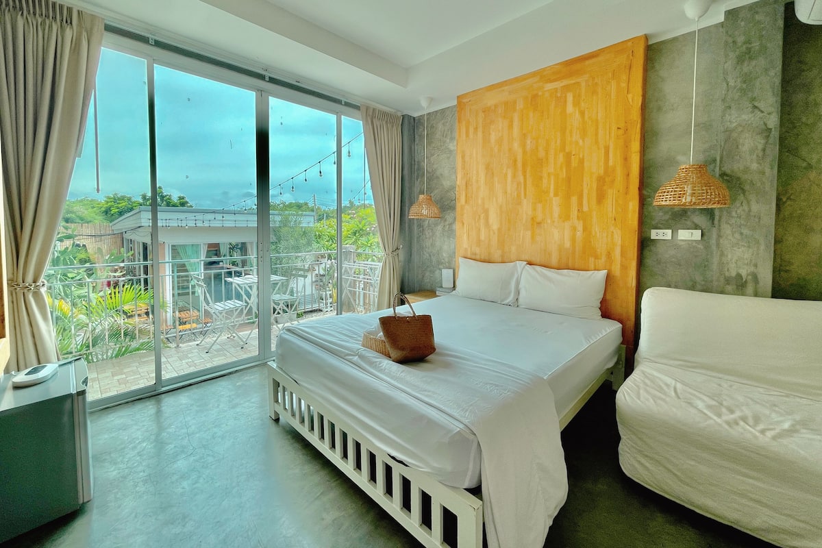 A modern bedroom with a large bed, a view of the balcony, and a wooden accent wall.