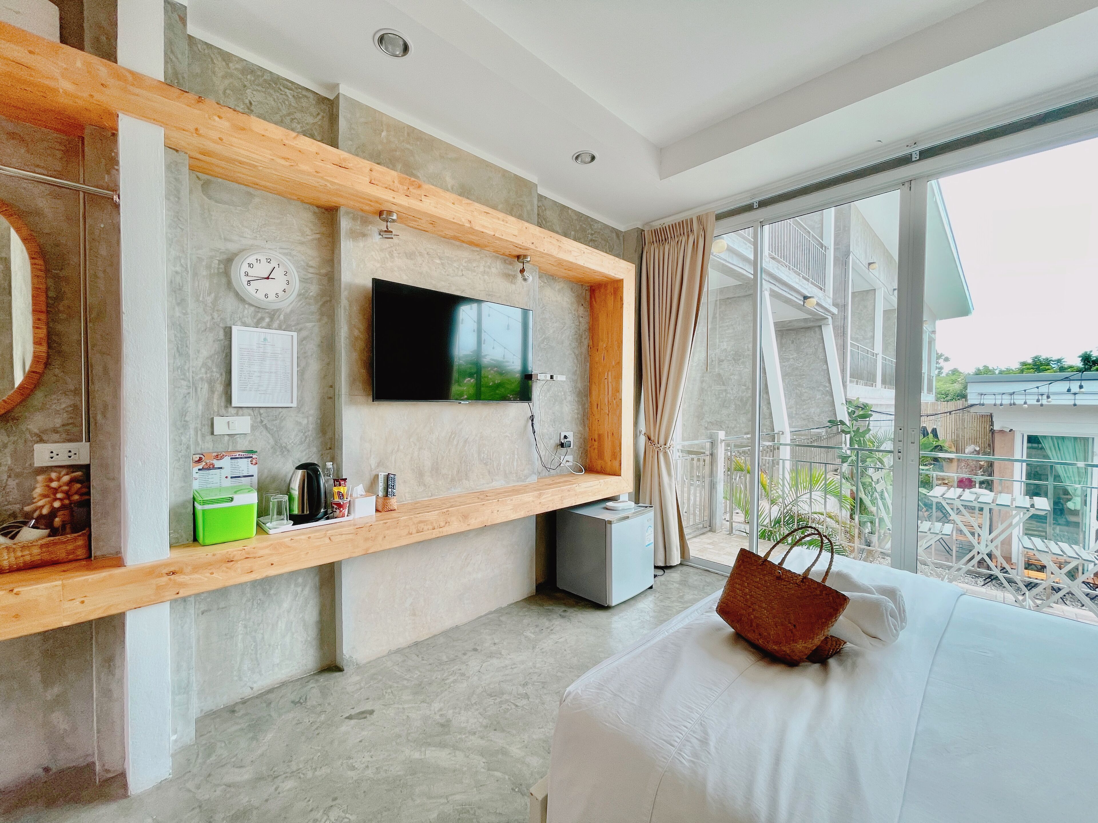 A modern hotel room with a large TV, wooden beams, a clock, and a view of the outdoors.