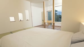 A modern hotel room with a large bed, a wooden floor, a window with a view, and a small table with a chair. - Ryokan Mokuzin (Hakuba)